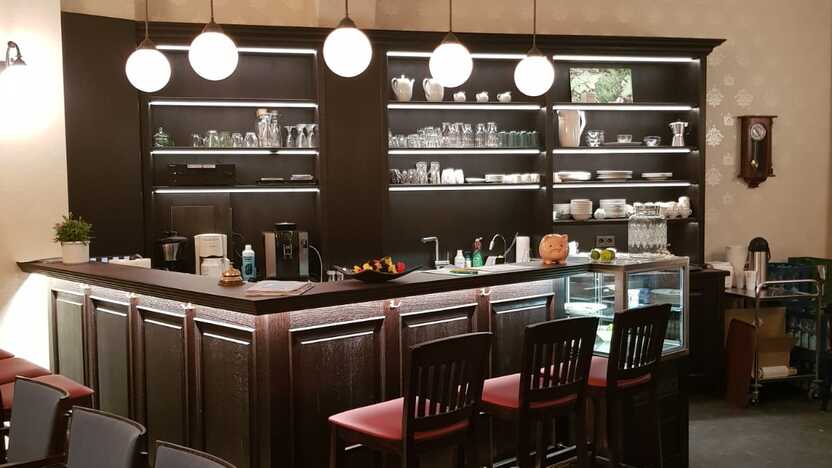 Barbereich mit Holztheke Dunkle Holztheke mit beleuchteten Regalen, Barhockern und Pendelleuchten in einem Salon.