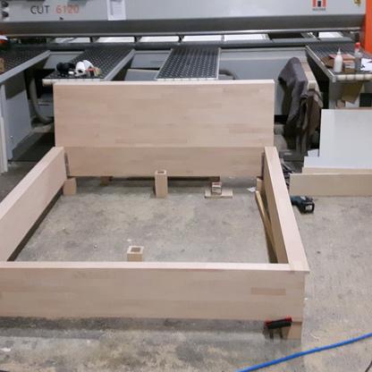 Bettgestell in der Werkstatt Helles Holzgestell wird in einer Tischlerei vor einer großen Zuschnittmaschine montiert.