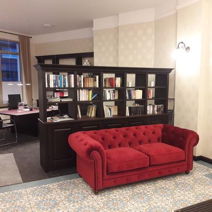 Elegantes Büro mit Bücherregal und rotem Sofa Stilvoll eingerichtetes Büro mit dunklem Bücherregal, voller Bücher, einem eleganten Schreibtisch und einem auffälligen roten Samtsofa.