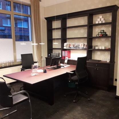Büro mit Wandregal Büro mit großem Schreibtisch, Hängelampen und dunklem Wandregal mit Stauraum und Ablageflächen.