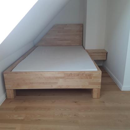 Maßgeschneidertes Bett unter einer Dachschräge Ein maßgefertigtes Holzbett, das perfekt unter eine Dachschräge passt, mit passendem Parkettboden. Optimale Raumnutzung für kleine Räume.