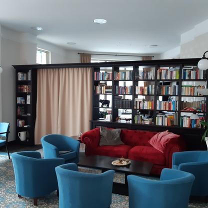 Wohnbereich mit Bücherregal Gemütlicher Wohnbereich mit rotem Sofa, blauen Sesseln und großer dunkler Bücherwand.