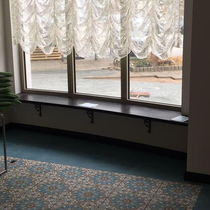Fensterbank mit dunkler Ablage Lange dunkle Fensterbank mit dekorativen Konsolen verläuft unter großen Fenstern mit Gardine.