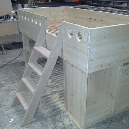 Holzbett mit Treppe in einer Werkstatt Unvollendetes Holzbett mit eingebauter Treppe und dekorativen Elementen in einer gut ausgestatteten Werkstatt.