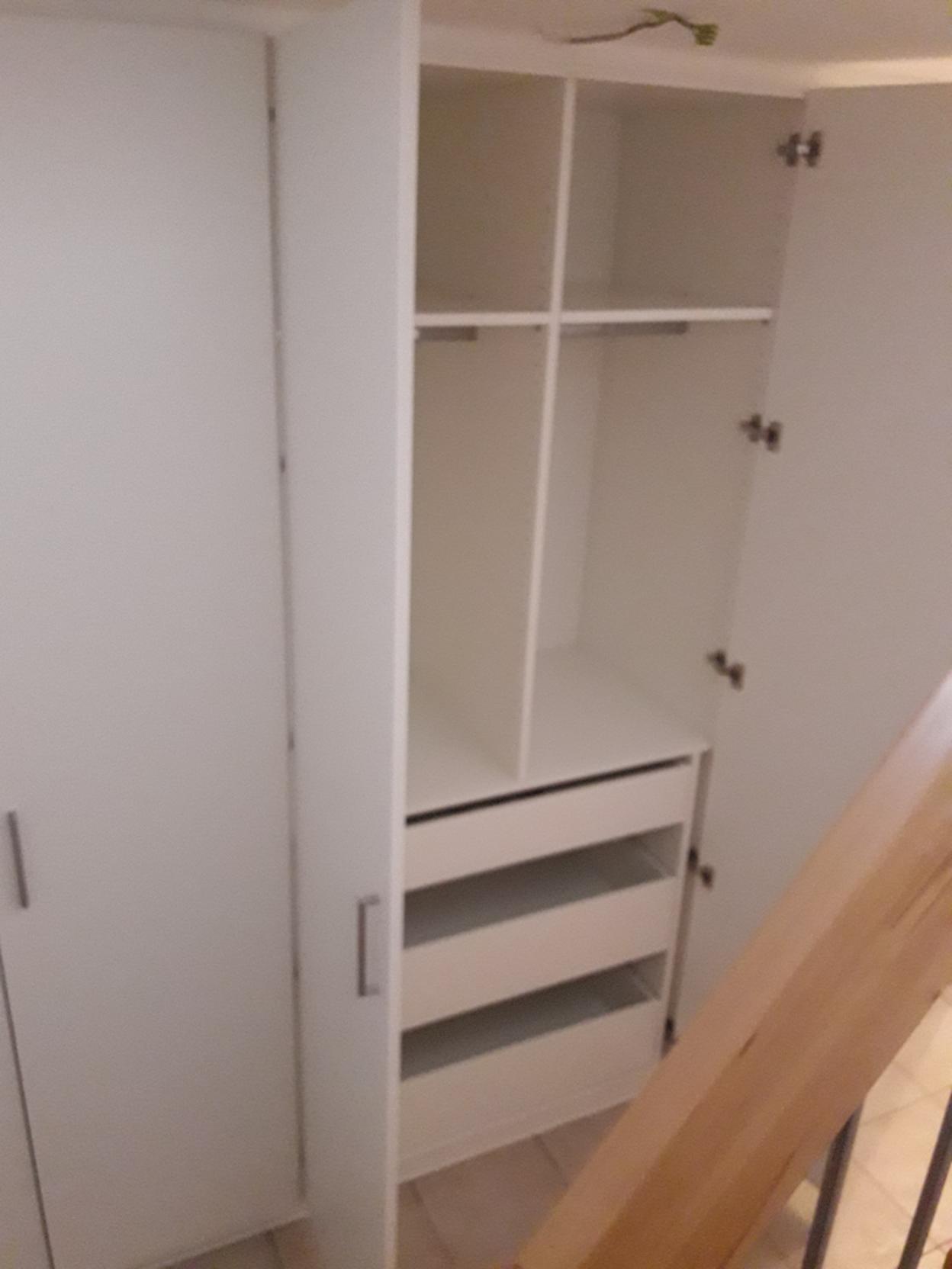 Maßgeschneiderter Einbauschrank in einer Ecke Ein großer, weißer Einbauschrank nach Maß, in einer Raumtiefe positioniert, bietet sowohl Regalfächer als auch Schubladen für optimierte Aufbewahrungslösungen.