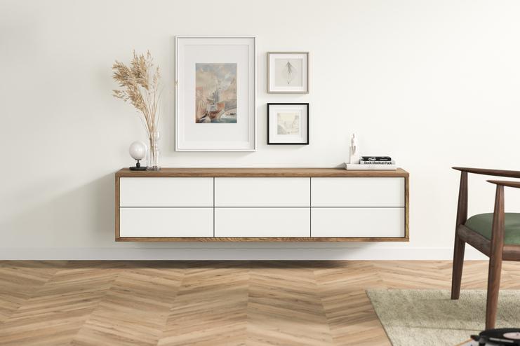 Maßgefertigtes Hängeboard im modernen Wohnbereich Ein minimalistisches, maßgefertigtes Hängeboard aus Holz mit weißen Schubladen, unter eingerahmten Bildern, verleiht diesem Wohnbereich ein stilvolles Flair.